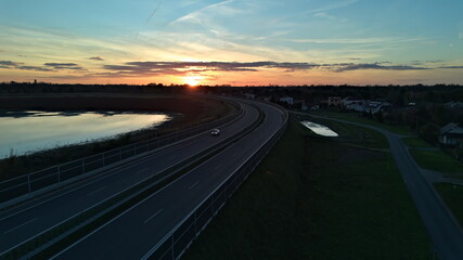 Car Driving on Curved Highway at Sunset by Lake.