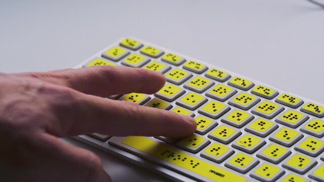 Computer keyboard with braille font alphabet. Blind person is typing words, hands. Technological device for visually impaired people. Tactilely touches bumps on keys. Inclusion, assistive technology