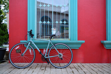 Bicycle parked beside red wall with turquoise window frame
