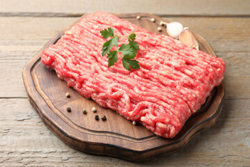 Raw minced meat with parsley and spices on wooden table, closeup