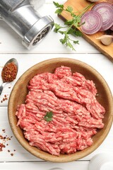 Raw minced meat, parsley, spices and grinder on white wooden table, flat lay