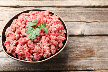 Fresh raw minced meat with parsley in bowl on wooden table, closeup. Space for text