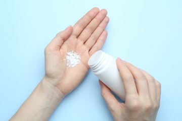 Woman with bottle of talcum powder on light blue background, top view