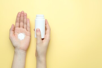 Woman with bottle of talcum powder on yellow background, top view. Space for text