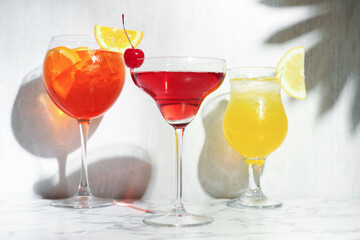 Glasses of tasty cocktails with garnish on white marble table