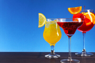 Glasses of tasty cocktails with garnish on wooden table against blue background, closeup. Space for text