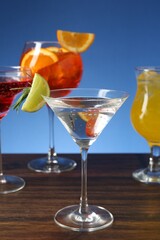 Glasses of tasty cocktails with garnish on wooden table against blue background, closeup