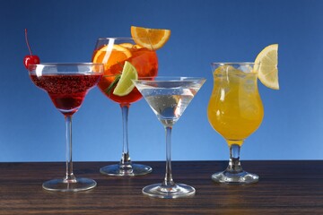 Glasses of tasty cocktails with garnish on wooden table against blue background
