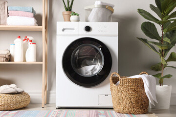 Washing machine with clothes, detergents and houseplants in laundry room. Interior design