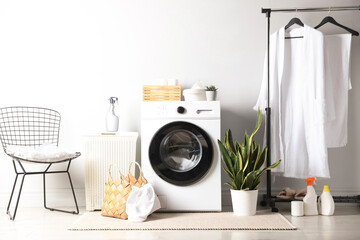 Washing machine with clothes, detergents and houseplants in laundry room. Interior design