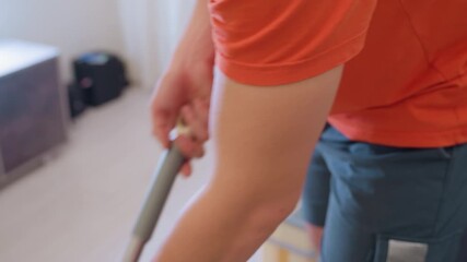 Close up of man in orange shirt and gray shorts gripping mop handle while cleaning floor indoors showing focus on household hygiene cleanliness and daily domestic routine