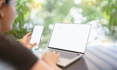 Woman using smartphone and laptop with blank white screens for mockup,Business woman working remotely in nature while travel. Ideal for technology, remote work, and digital communication concepts