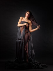 On a dark background is the figure of an attractive woman dressed in a black robe. Her bare shoulders and chest are covered with her hand, and she is wearing only panties.