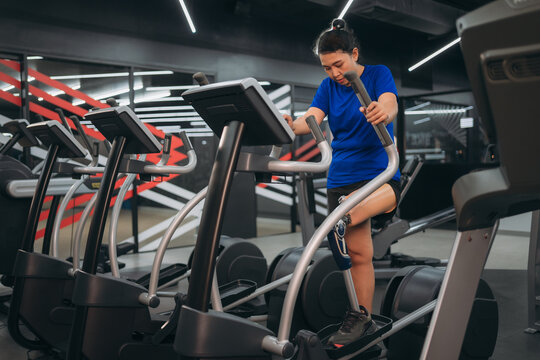 A motivated woman with a prosthetic leg walking on a treadmill in a modern gym, representing fitness, rehabilitation, and strength with a positive attitude towards an active healthy lifestyle.
