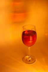 Elegant wine glass filled with red liquid on a warm golden-yellow background. Abstract lighting creates a luxurious and artistic mood, perfect for concepts of celebration, elegance, and nightlife.