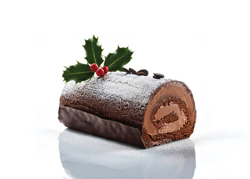 classic French B&ucirc;che de No&euml;l chocolate Yule log cake, decorated with cream, chocolate bark texture, holly leaves, and powdered sugar, isolated on white background