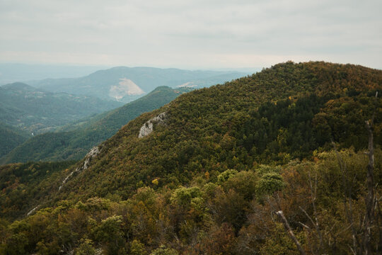 Wide view of forested mountain ridges with colorful autumn foliage and distant hills under cloudy sky. View from Kablar mount