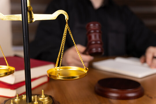 A person, likely a judge,is seated at a desk with a gavel and a scale of justice