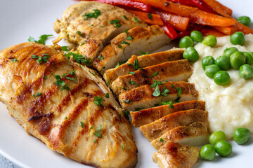 Grilled chicken breast slices served with mashed potatoes and vegetables.