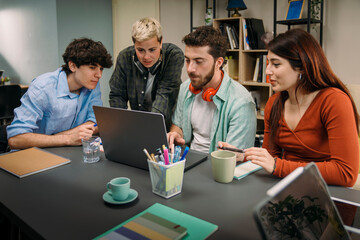 Group of diverse gen z students working together on laptop in a creative office. Concept of...