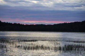 A panoramic view of a sunset over a wilderness lake in the Adirondacks with red and gold colors.
