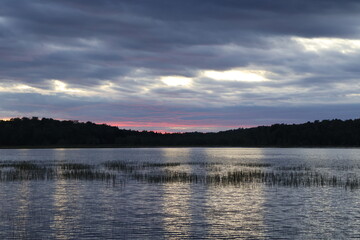 A panoramic view of a sunset over a wilderness lake in the Adirondacks with red and gold colors.