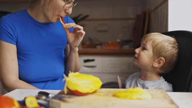 Mother and son eating fresh mango in the kitchen