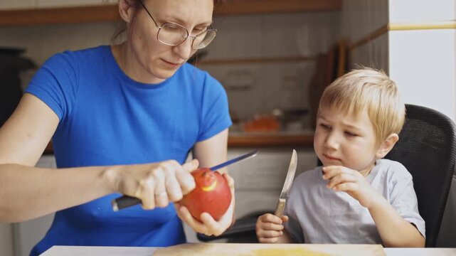Mother peeling mango fruit for her son in the kitchen