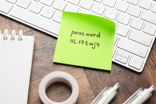 Sticky note with password, keyboard and stationery on wooden desk, closeup