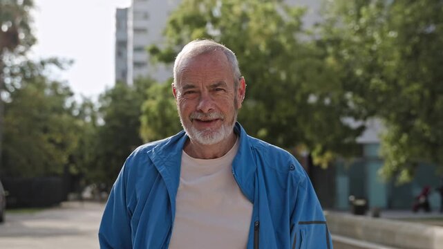 Happy senior man wearing blue sport wear looking to camera after morning workout in the city