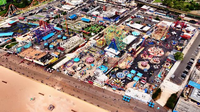 Amusement park near beach with roller coasters and carnival rides. Aerial view of various colorful attractions from above.