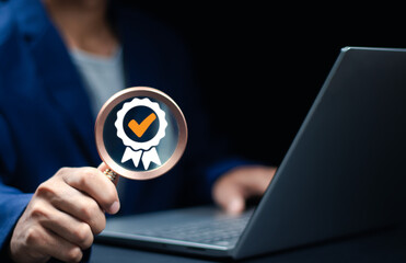 businessperson holding magnifying glass showing verified badge while working on laptop. Concept of quality assurance, data validation and trust symbol in digital business.