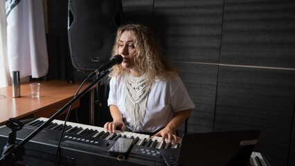 Caucasian woman singing into microphone and playing synthesizer. 