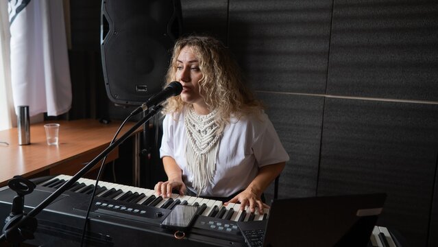 Caucasian woman singing into microphone and playing synthesizer.