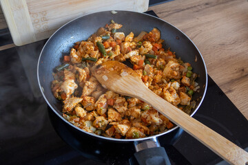 Chicken and vegetables frying in a non-stick pan on a stove with a wooden spatula. Warm light highlights the home-cooking process, ideal for food blogs, recipes, and kitchen lifestyle content.