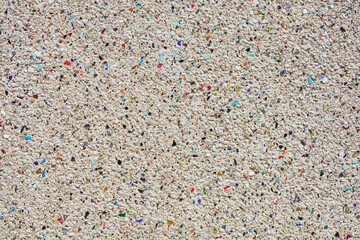 Heller grober Putz mit eingearbeiteten grauen und farbigen Steinen, teilweise aus Glas - Nahaufnahme einer Fassade