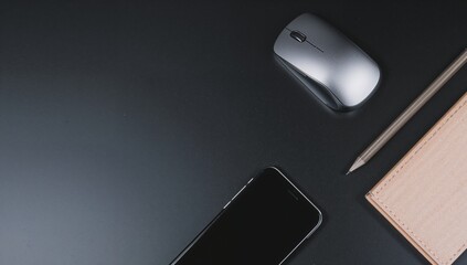 Sleek workspace setup with modern phone, mouse, pen, and notepad on dark surface