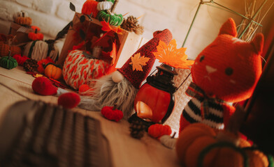 Naklejka premium Warm cozy autumn home scene with handmade knitted pumpkins, soft toys, pinecones, and orange lantern light, creating festive fall or Halloween interior decoration vibes.