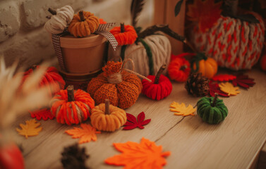 Cozy autumn composition with handmade knitted pumpkins, colorful felt leaves, pinecones, and rustic decor on a wooden surface, creating a warm fall seasonal atmosphere.
