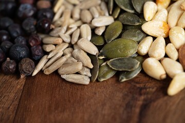 Obraz premium A vibrant assortment of seeds, including sunflower seeds, pumpkin seeds, pine nuts, and wild berries, arranged artfully on a wooden surface.