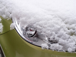 Close-up of a green car headlight partially covered in fresh snow, realistic photo style, with a soft natural outdoor snowy background