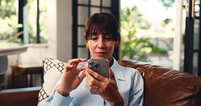 Mature woman, phone and texting on sofa in home, relax and notification for web chat in living room. Person, smartphone and smile on couch with mobile app, contact or social network at apartment