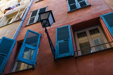 Low angle view of a traditional old building with vibrant blue shutters and a vintage street lamp in Nice, France.