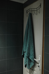 Soft green towel on hook inside modern tiled bathroom. Perfect for home, lifestyle, and hygiene related visuals