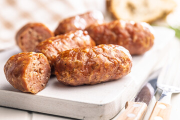 Photo of roasted italian sausage salsiccia on cutting board on white table.