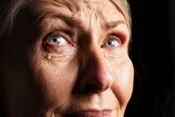 Obraz premium Senior woman crying on black background, closeup