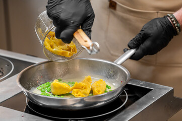Chef cooking tortellini with peas and cream sauce in a modern kitchen. Close-up of pasta preparation with strainer, frying pan, and induction cooktop. Culinary process concept.
