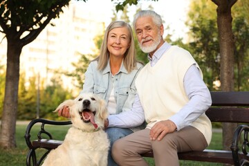 Portrait of happy senior couple with adorable Golden Retriever dog on bench outdoors
