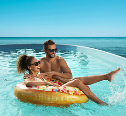 Couple having fun in swimming pool with infinity view on ocean