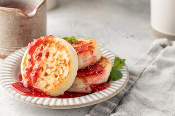 Cottage cheese pancakes or syrniki with raspberry jam on ceramic plate on light gray kitchen table. Healthy sweet breakfast
